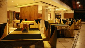 A restaurant with tables and chairs covered in yellow tablecloths, wooden paneling on the walls, and ceiling fans.