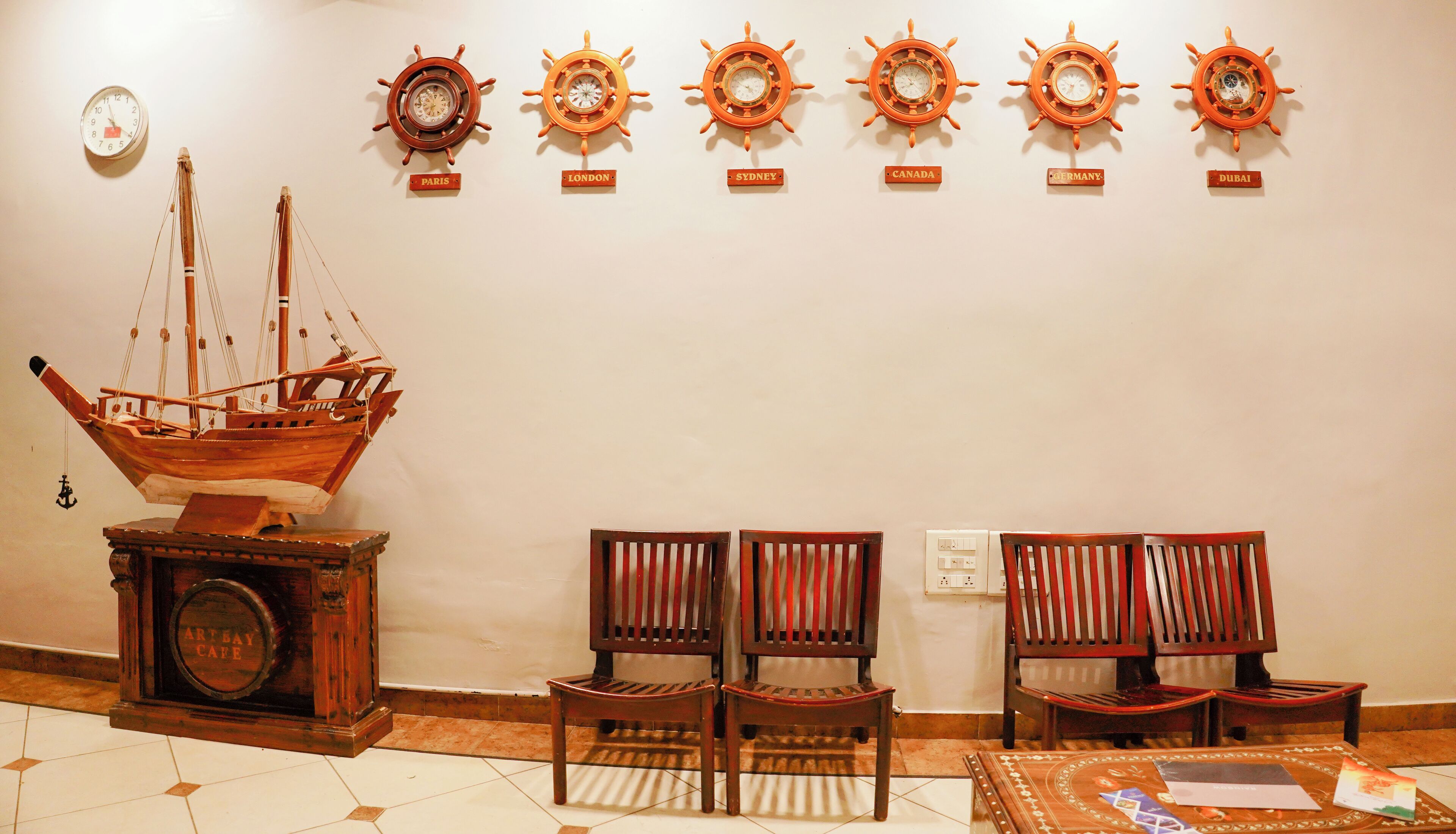 A room with a wooden ship model, a wall clock, and six ship wheel clocks labeled with city names.