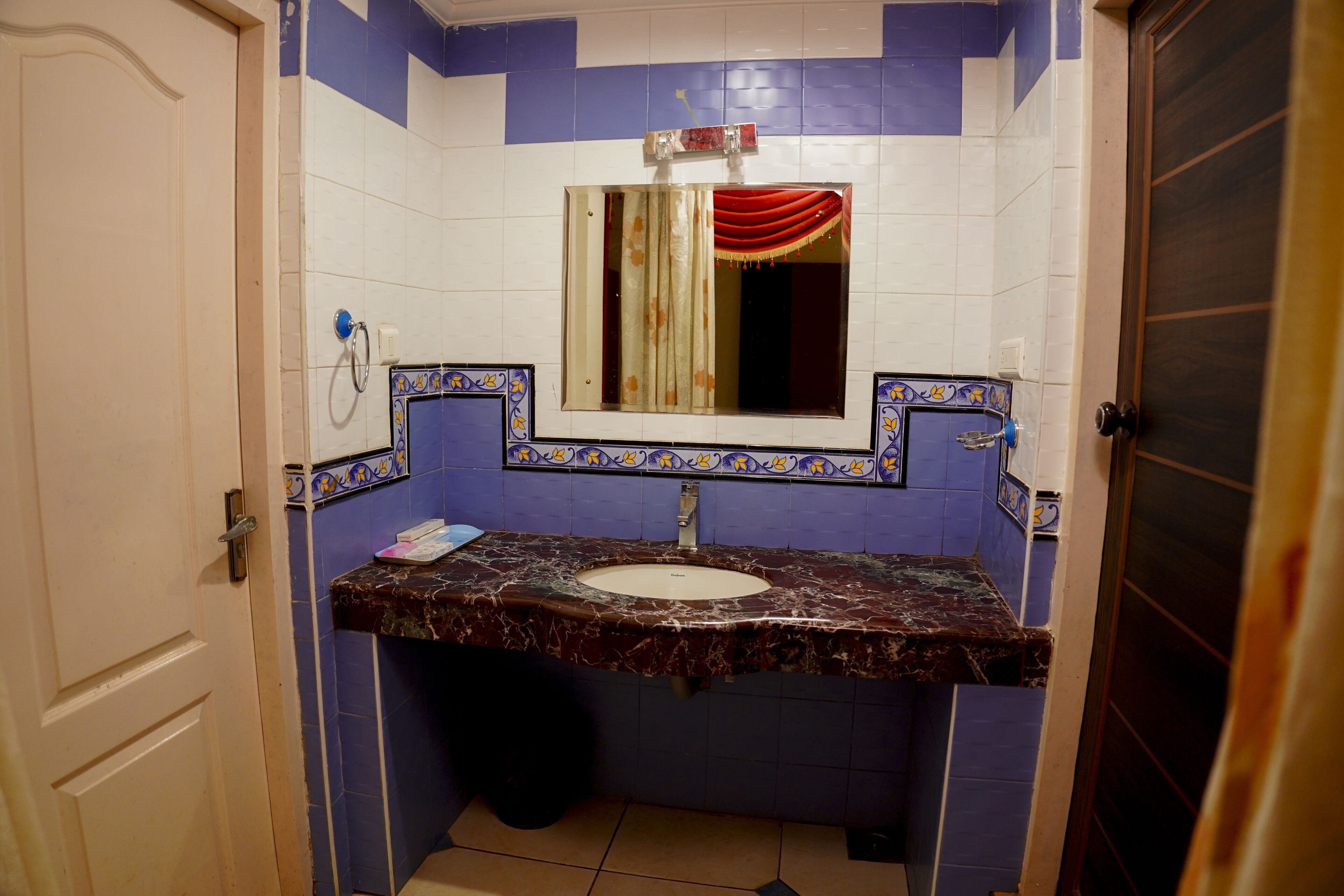 A bathroom with a marble sink, a mirror with a red curtain, and blue and white tiled walls.