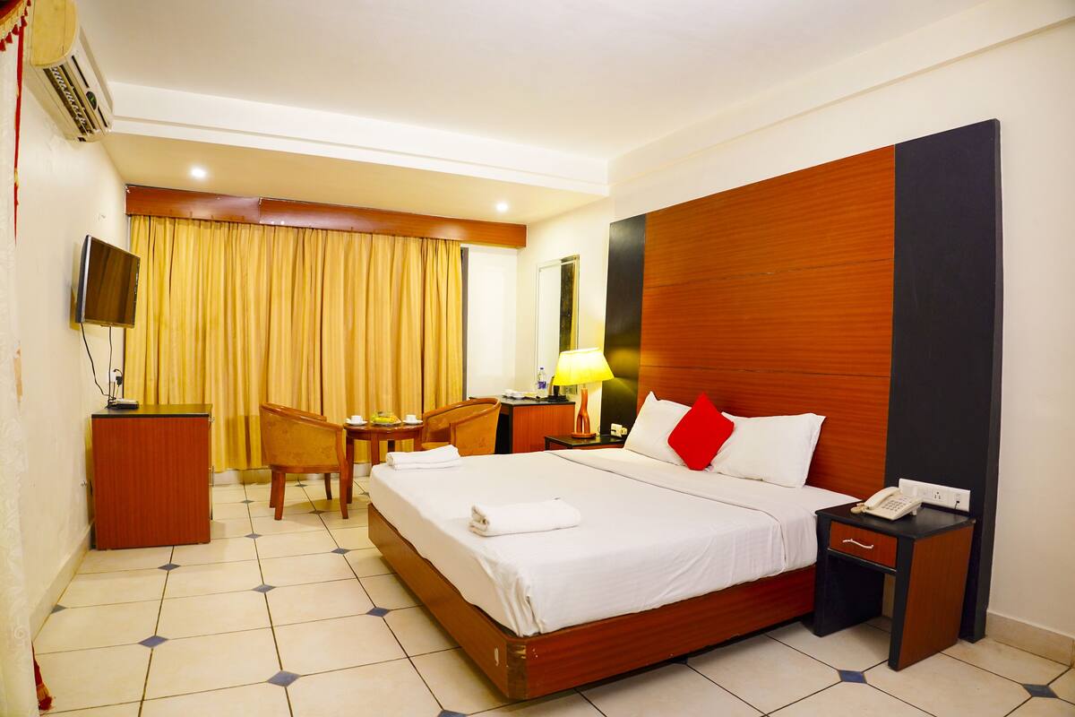 A hotel room with a large bed, a desk with a chair, a TV, a lamp, and a telephone.
