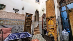 Un interior tradicional marroquí con elaborados trabajos en azulejos, una puerta de madera y una escalera que conduce a un nivel superior.