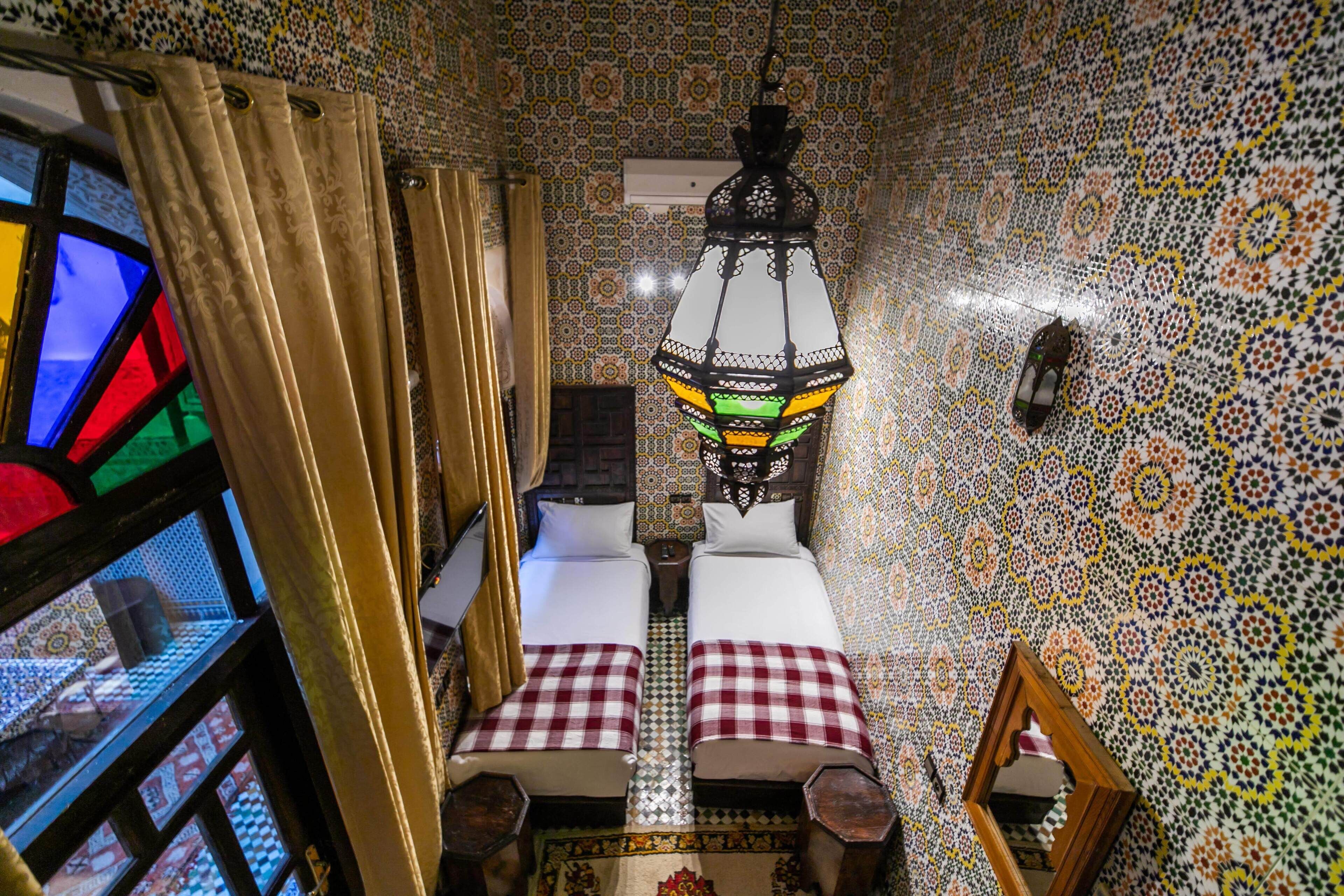 A room with two beds, a hanging lantern, and a stained glass window.