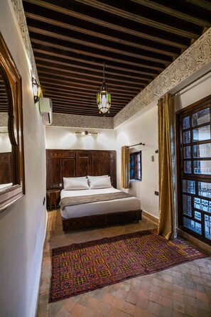 A bedroom with a large bed, a patterned rug, and a window with curtains. - Riad Fes Aicha & SPA (Fes)