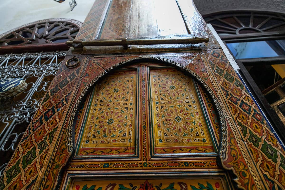 A detailed view of a wooden door with intricate geometric and floral patterns, part of a building's exterior.