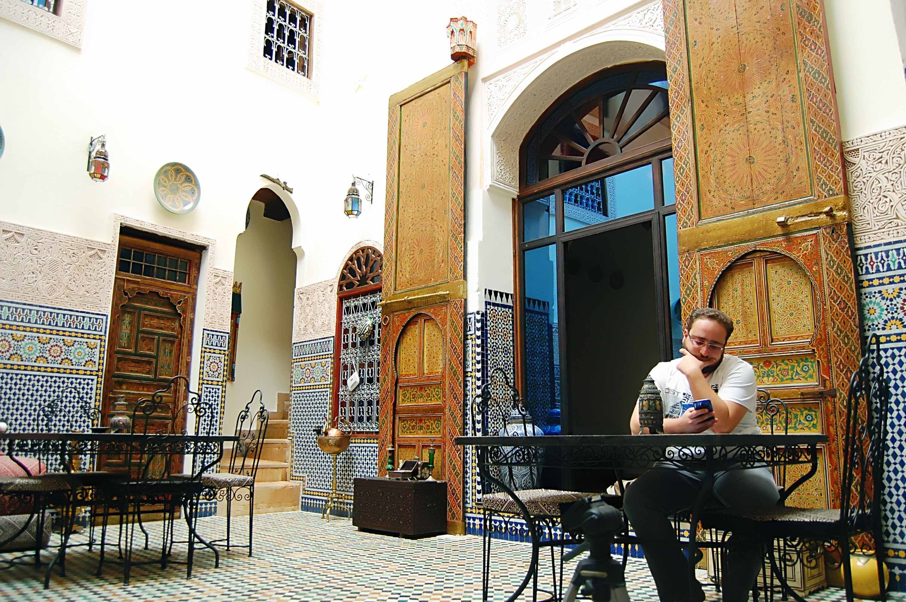A courtyard with ornate doors, tiled walls, and a person sitting at a table.