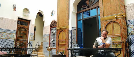 A courtyard with ornate doors, tiled walls, and a person sitting at a table.
