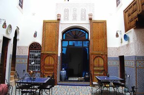 An interior with a large wooden door, patterned walls, and two tables with chairs. - Riad Fes Aicha & SPA (Fes)
