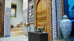 Un interior tradicional marroquí con un suelo de baldosas estampadas, puertas de madera ornamentadas y un gran jarrón azul y blanco.