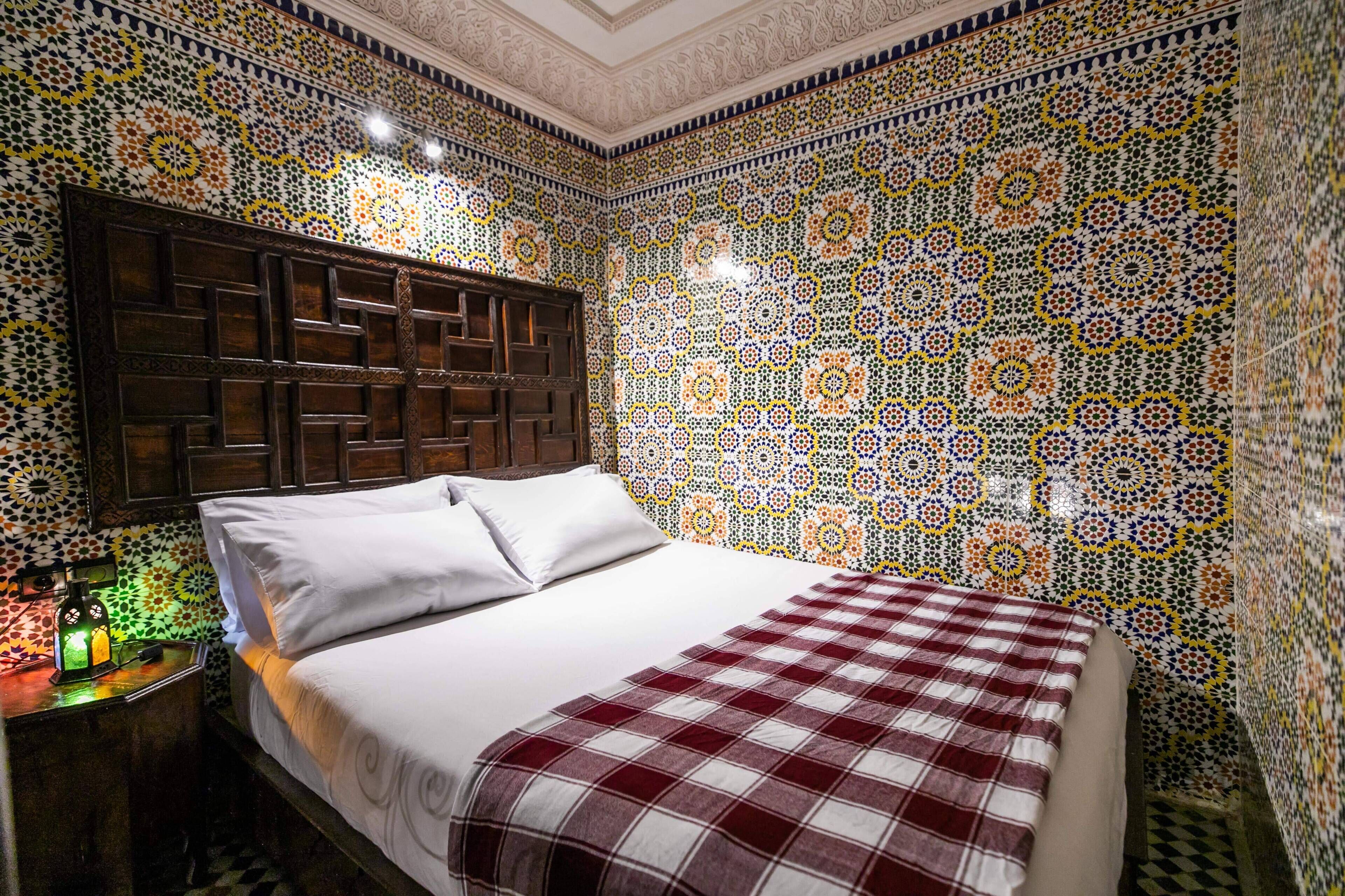 A room with a bed, a wooden headboard, and a nightstand with a lamp.