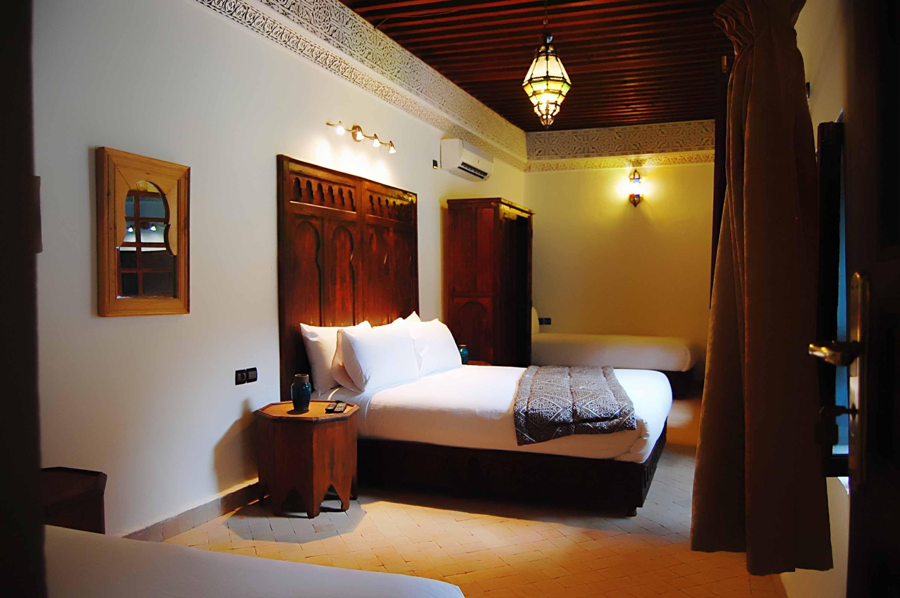 Una camera d'hotel con un letto grande, una testiera in legno, un comodino e un'unità di climatizzazione a muro, oltre a una lampada a sospensione.
