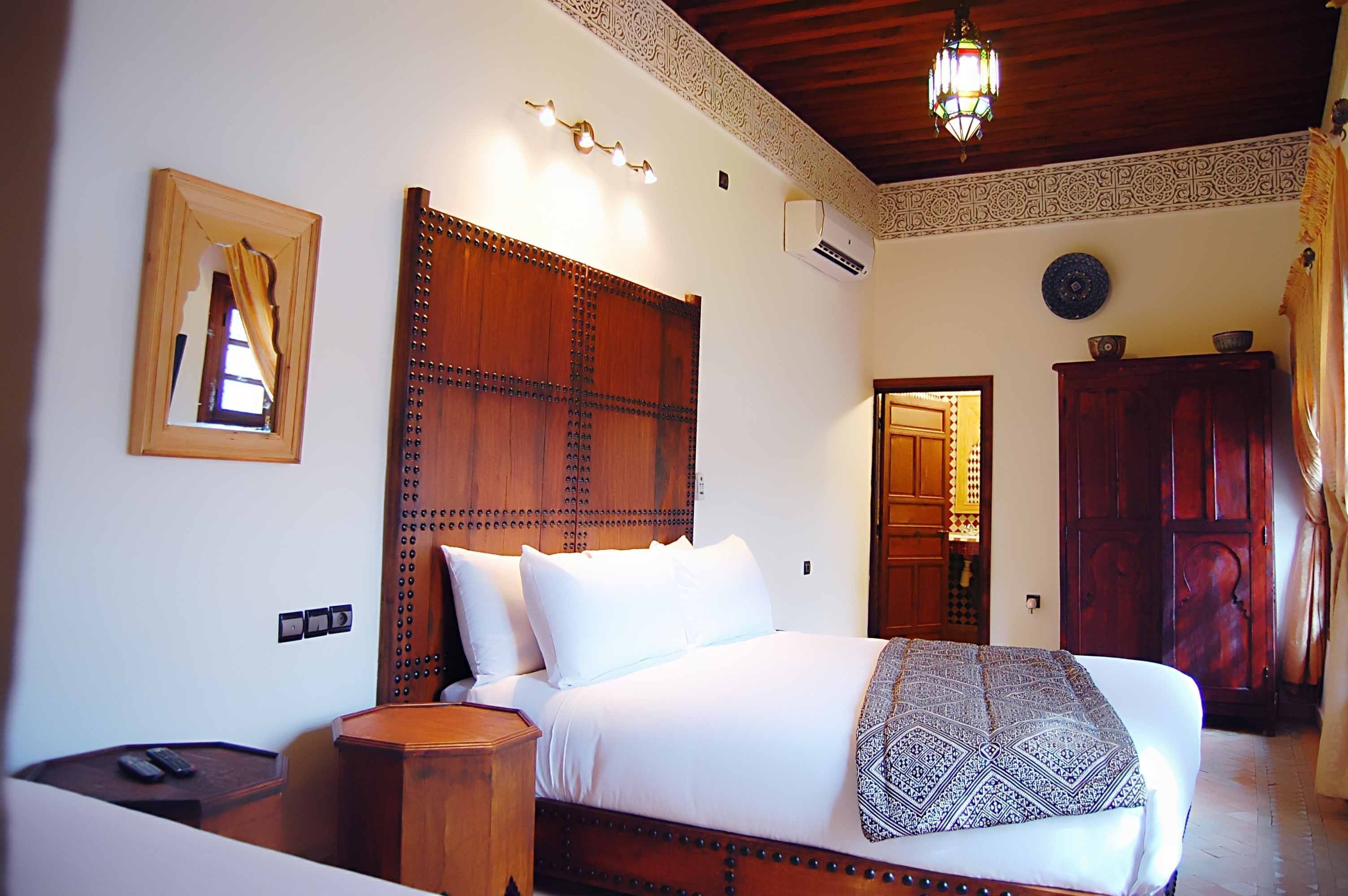 Un dormitorio con cabecera de madera, una cama con ropa de cama blanca, una mesita de noche y otro mueble auxiliar.