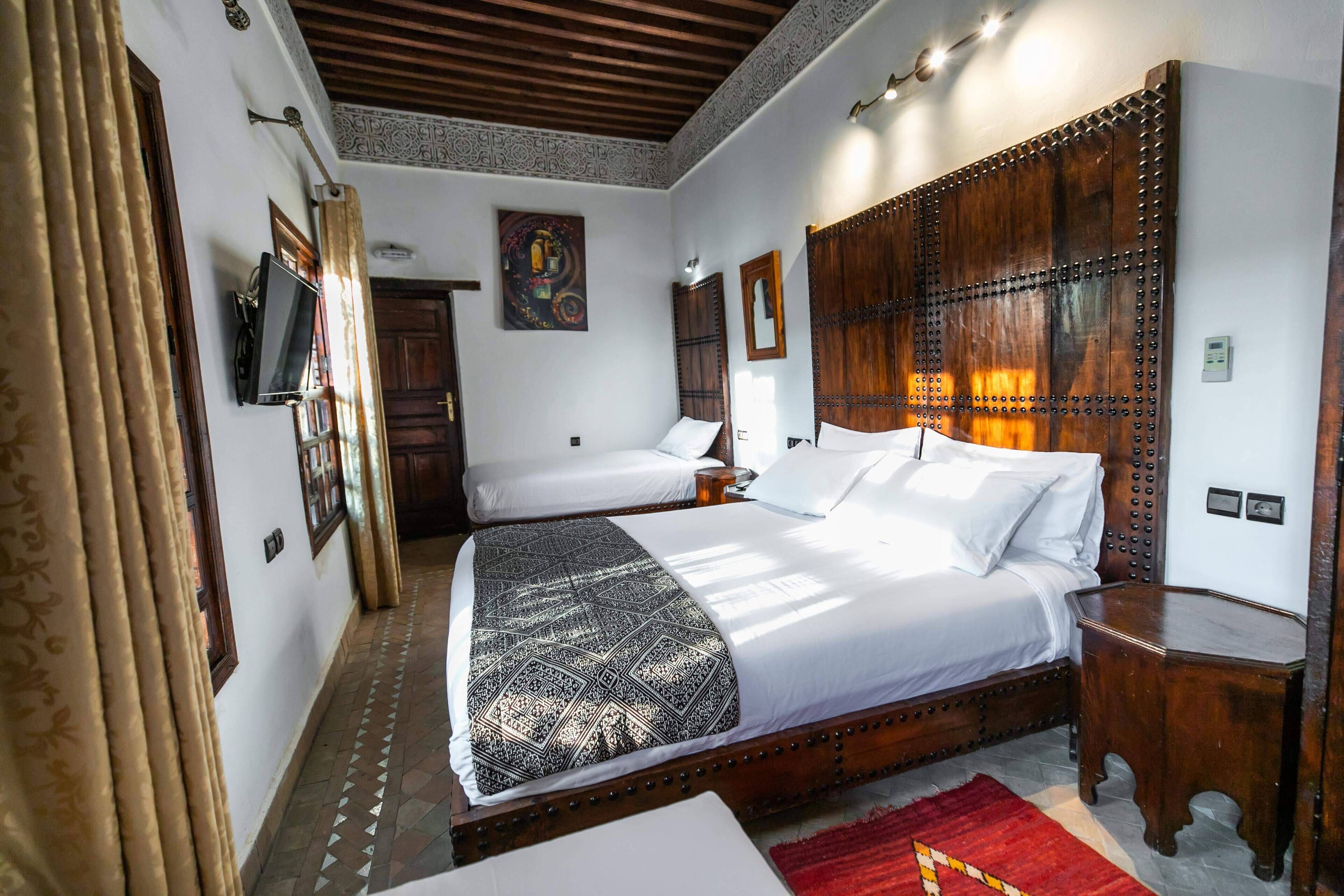 Une chambre d’hôtel avec un grand lit, un plus petit lit, une télévision et une tête de lit en bois.