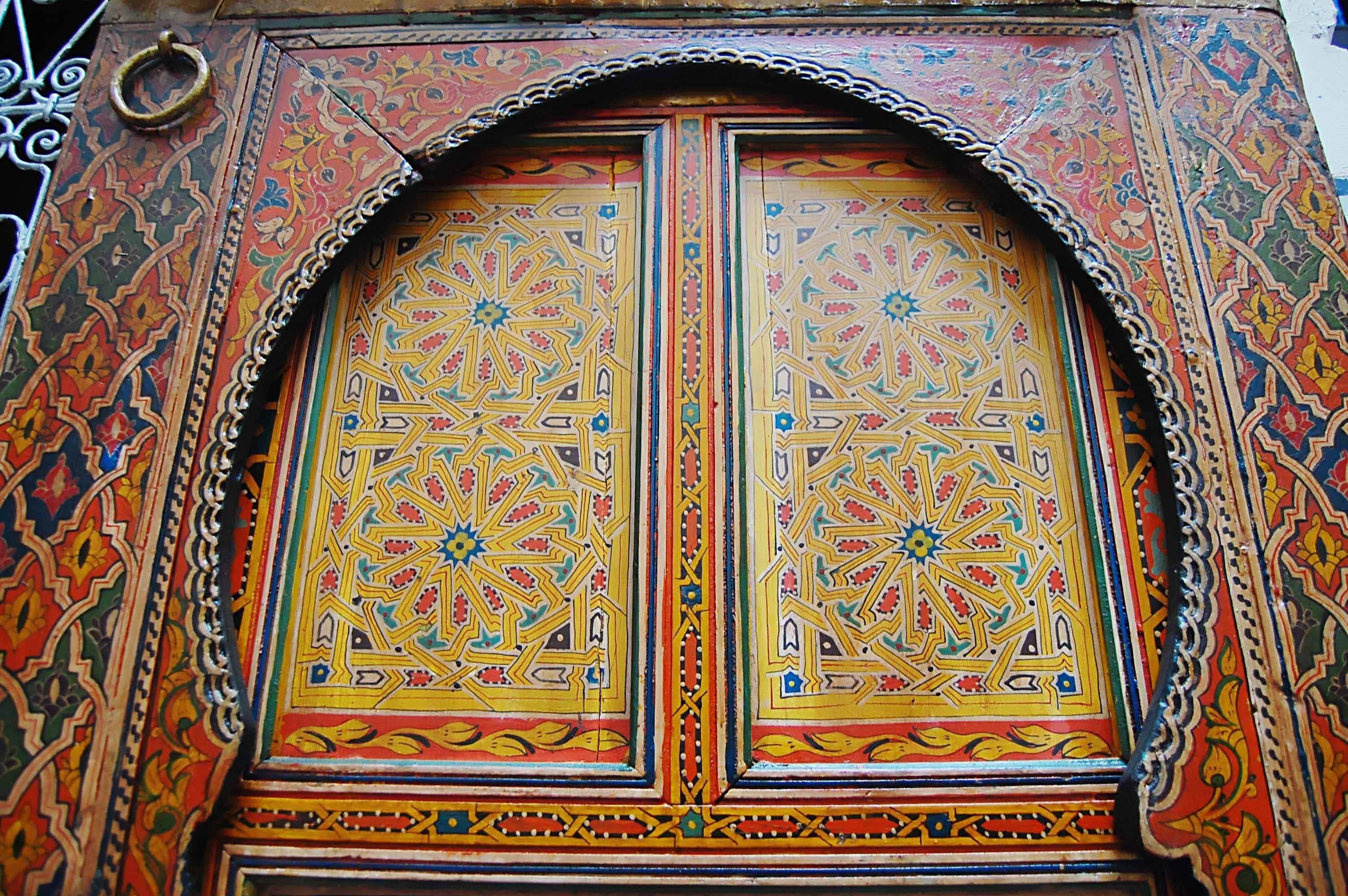 Une porte richement décorée et travaillée dans les moindres détails, ornée de motifs géométriques complexes et surmontée d’un arc décoratif.