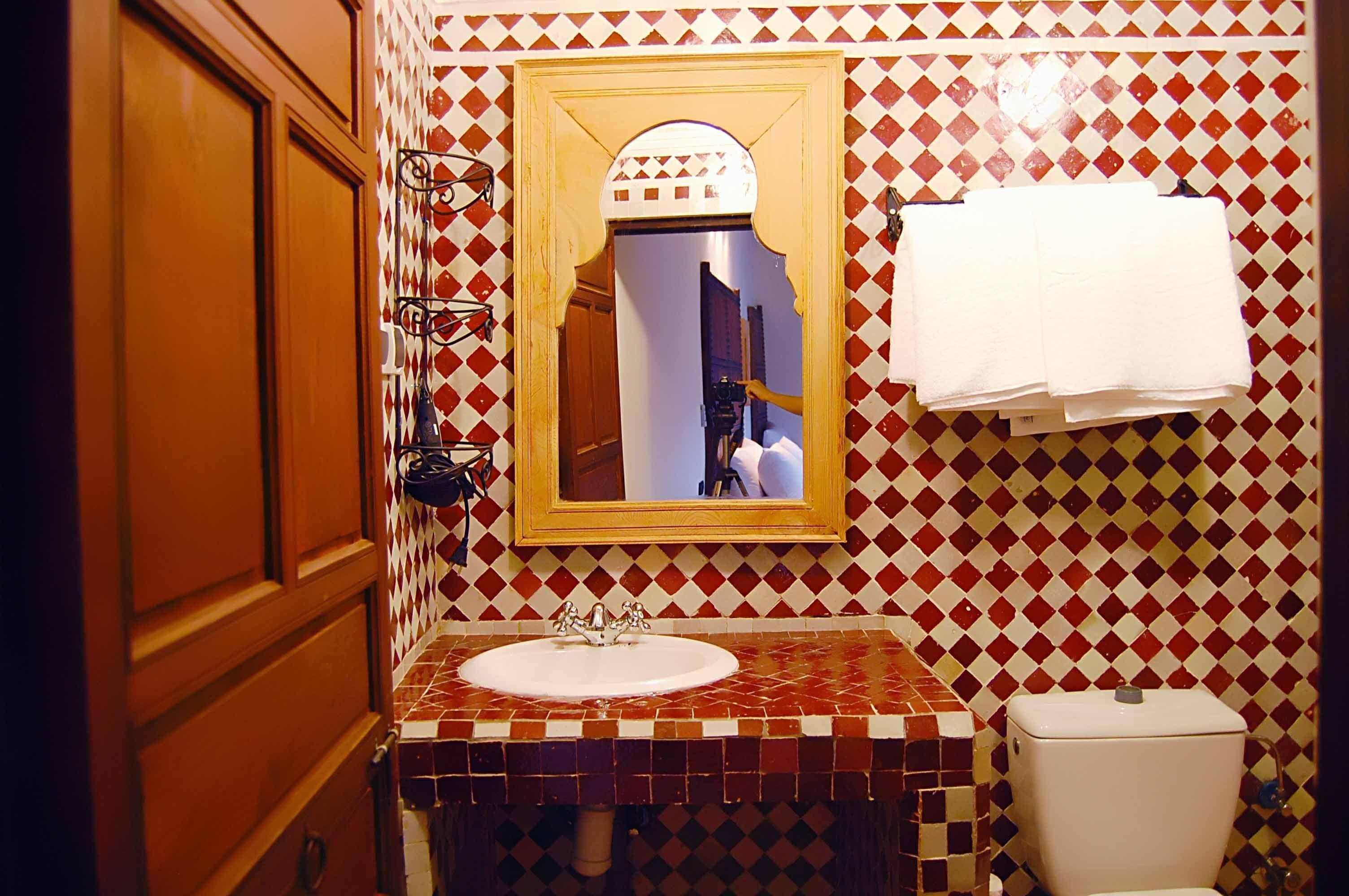 A bathroom with a checkered tile wall, a sink with a mirror, and a toilet.