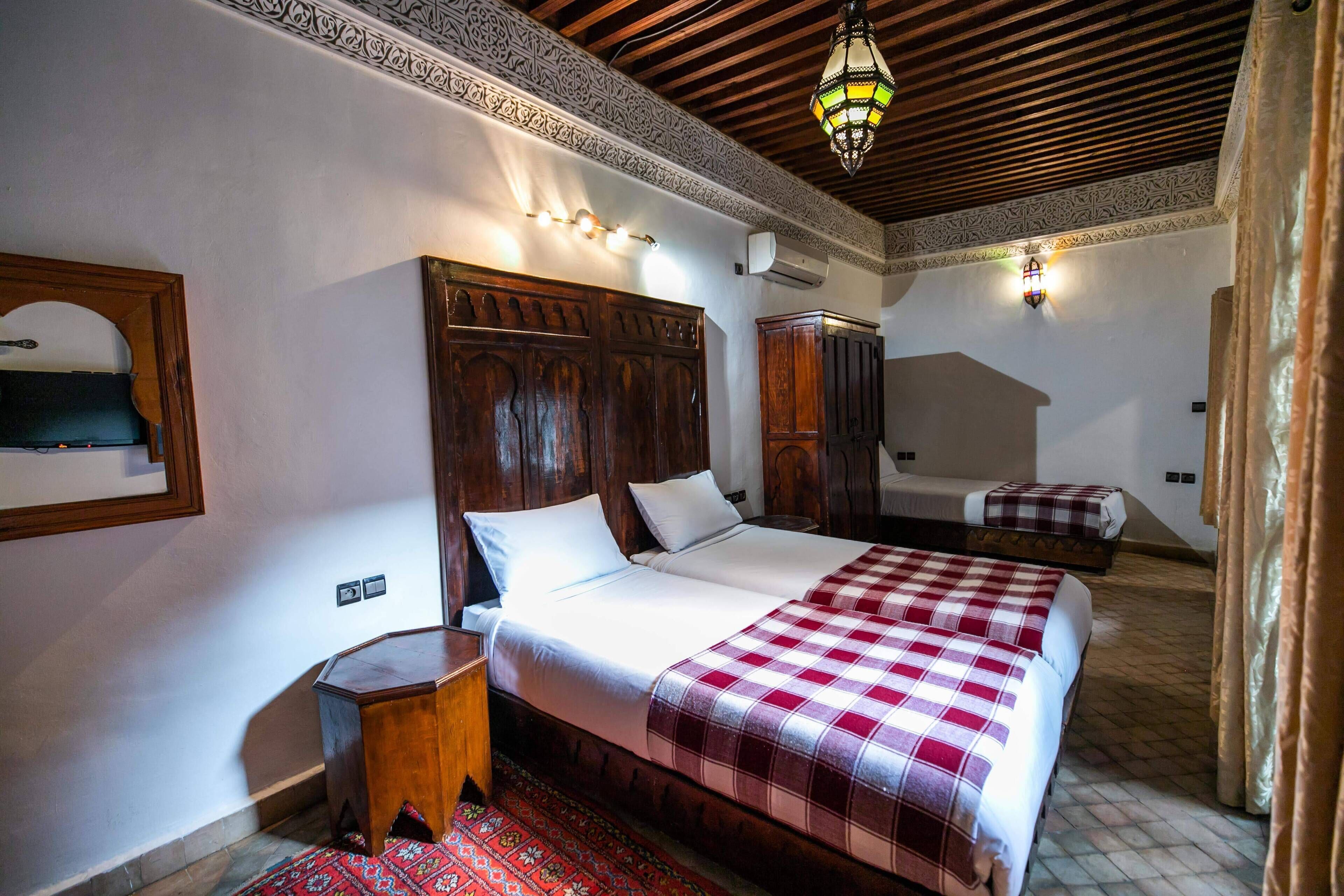 Habitación de hotel con una cama grande, una cama más pequeña, un armario de madera, una mesita de noche y una alfombra estampada.