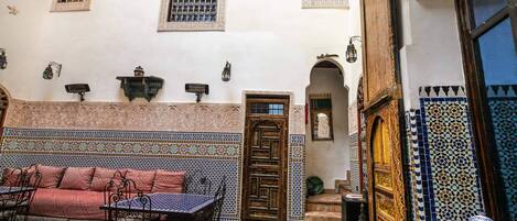 A traditional Moroccan interior with a patterned wall, a wooden door, a sofa, and a table with chairs.