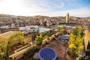 A rooftop terrace with potted plants, outdoor seating, and a view of a historic cityscape. - Riad Fes Aicha & SPA (Fes)