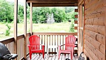 A wooden deck with two red Adirondack chairs and a black bench.