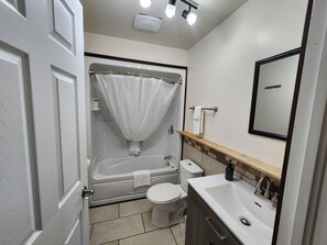 A bathroom with a bathtub, toilet, sink, and a mirror. - Ingonish Chalets (Ingonish)