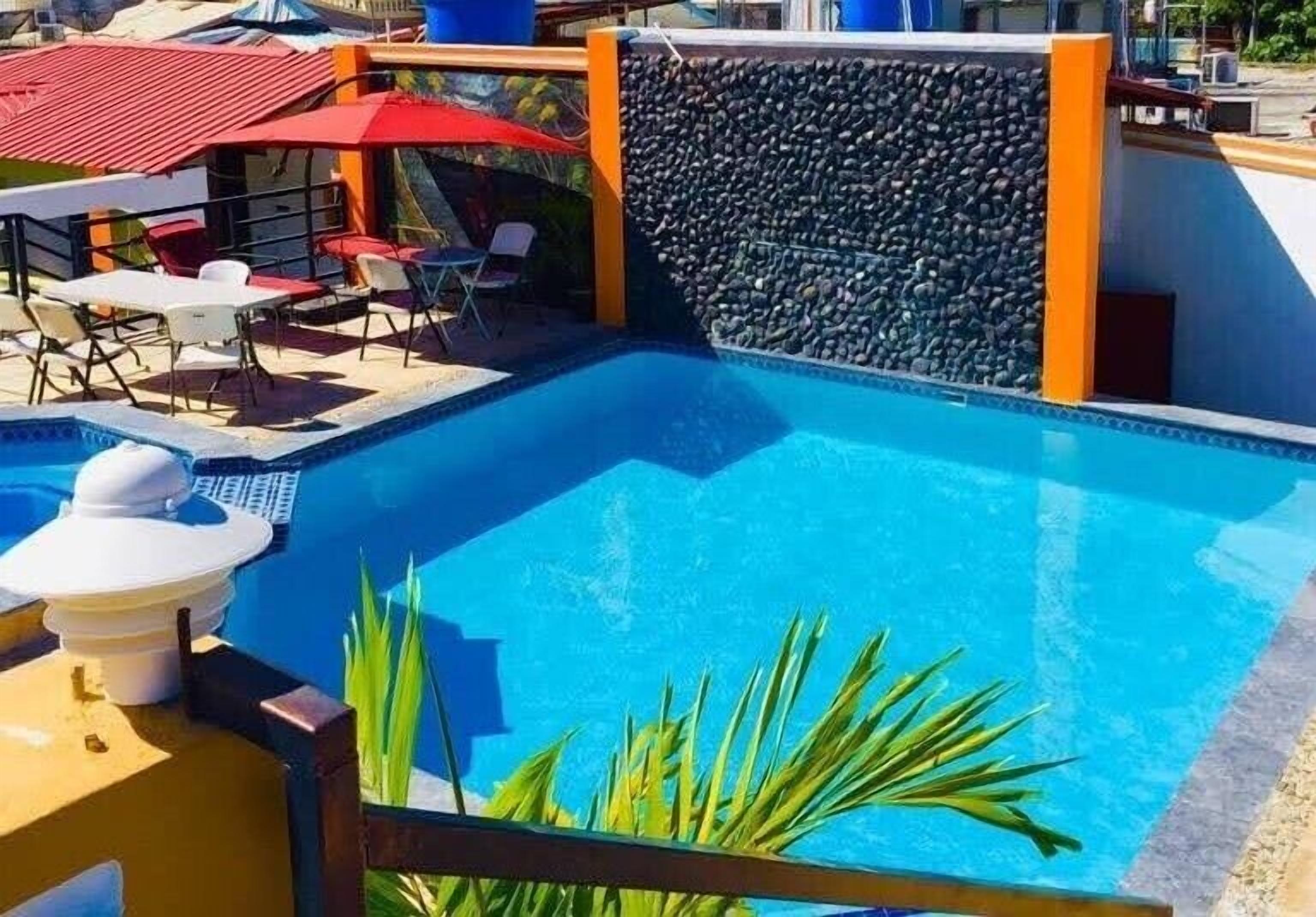 A swimming pool with a stone wall and a red umbrella.
