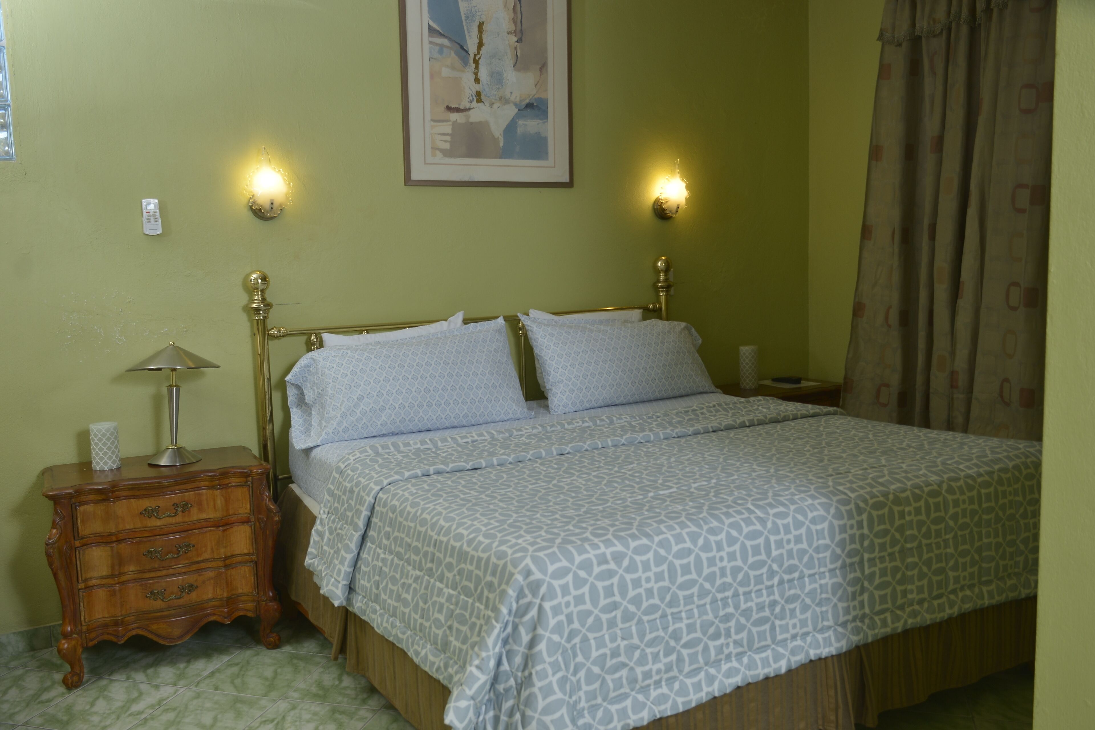 A bedroom with a bed, nightstand, lamp, and wall-mounted light.