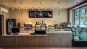 A café with a menu board, espresso machines, a display case with pastries, and a vending machine.