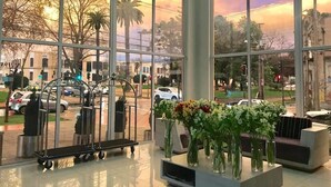 A spacious lobby with large windows offering a view of the street and surrounding buildings. There are several vases with flowers on a reception desk.