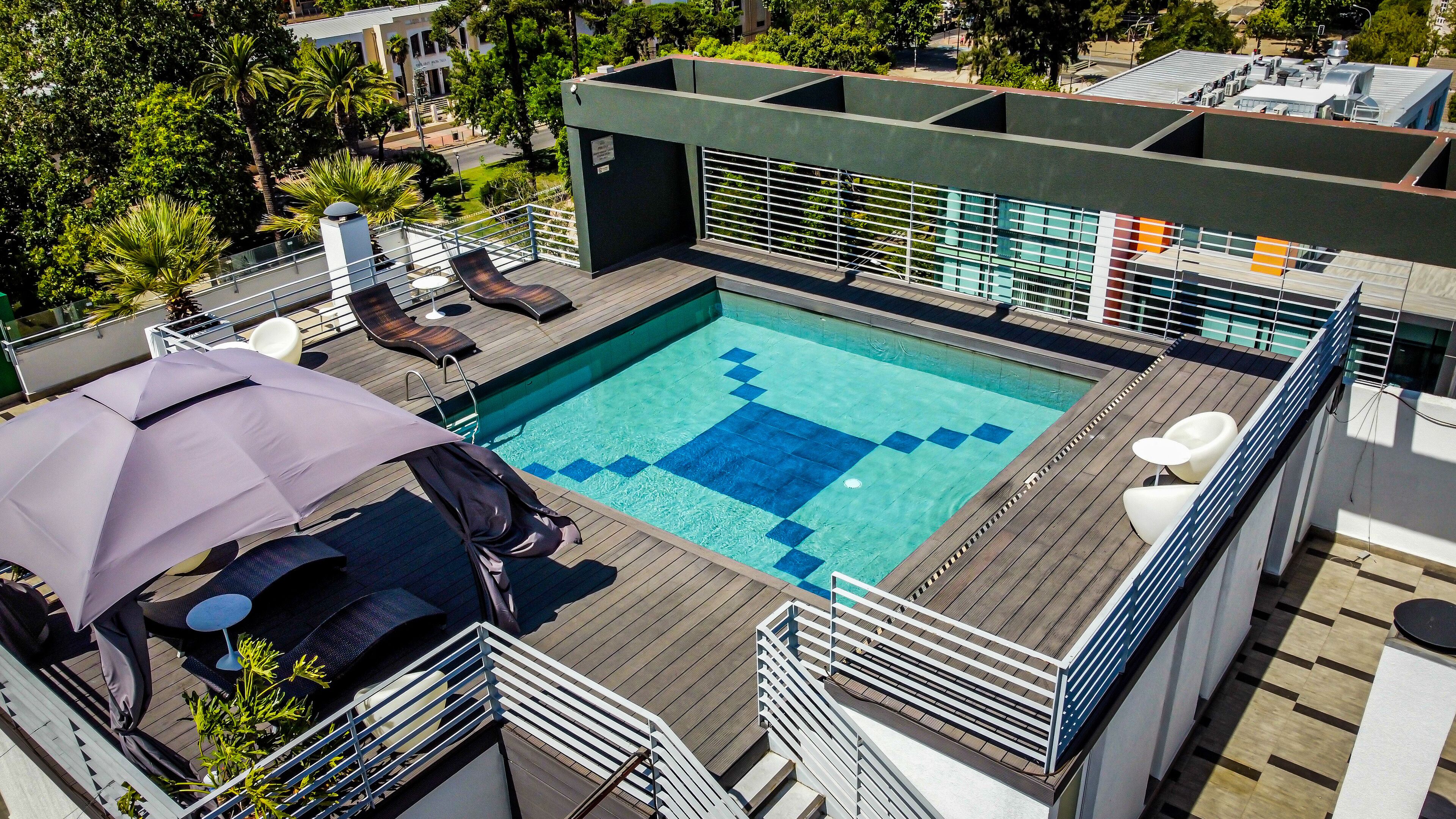 Una piscina en la azotea con terraza de madera, sillas de descanso y sombrillas.