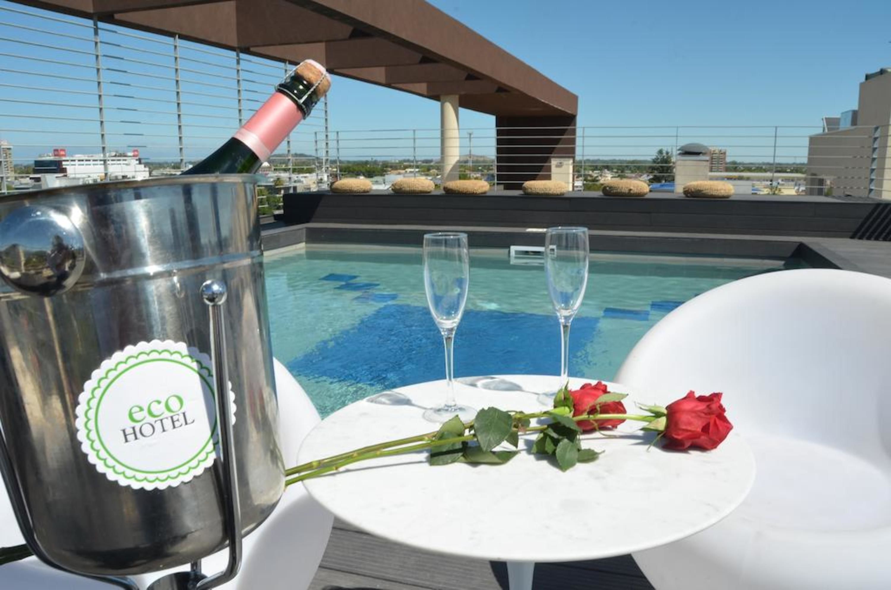Een dakzwembad met champagnekoeler, waarop 'eco hotel' staat, en twee glazen op een tafel met rozen.