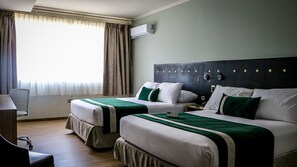 A hotel room with two beds, a desk, a chair, and a window with curtains.