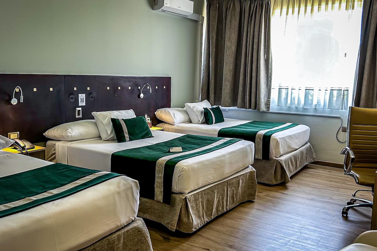 Habitación de hotel con dos camas, un escritorio, una silla y un ventanal con cortinas.