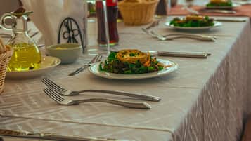 Una mesa servida con platos de comida, cubiertos, una botella de aceite y una cesta.