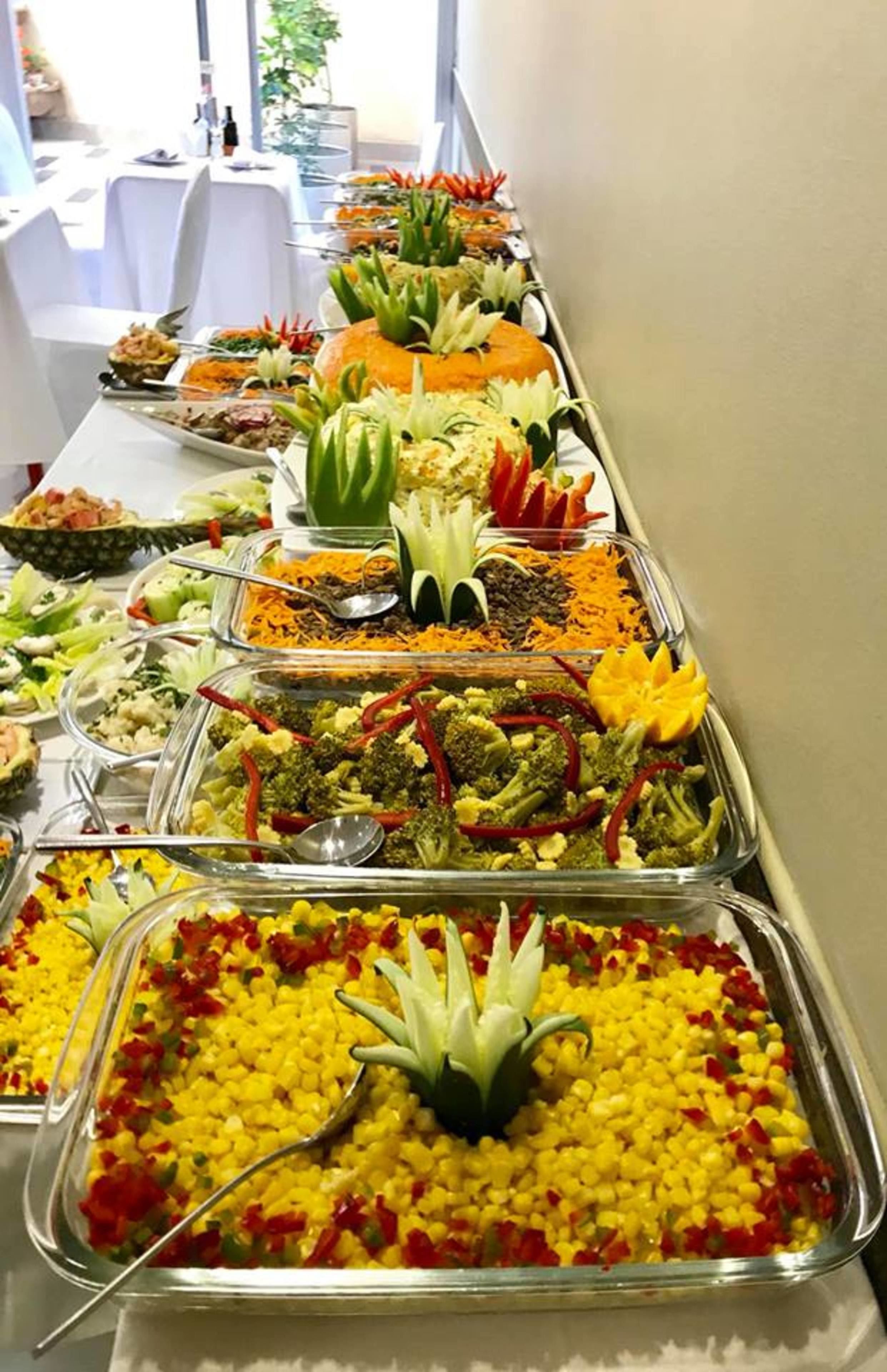 Un bufé con diferentes alimentos dispuestos en bandejas, entre ellos frutas, verduras y otros platos.