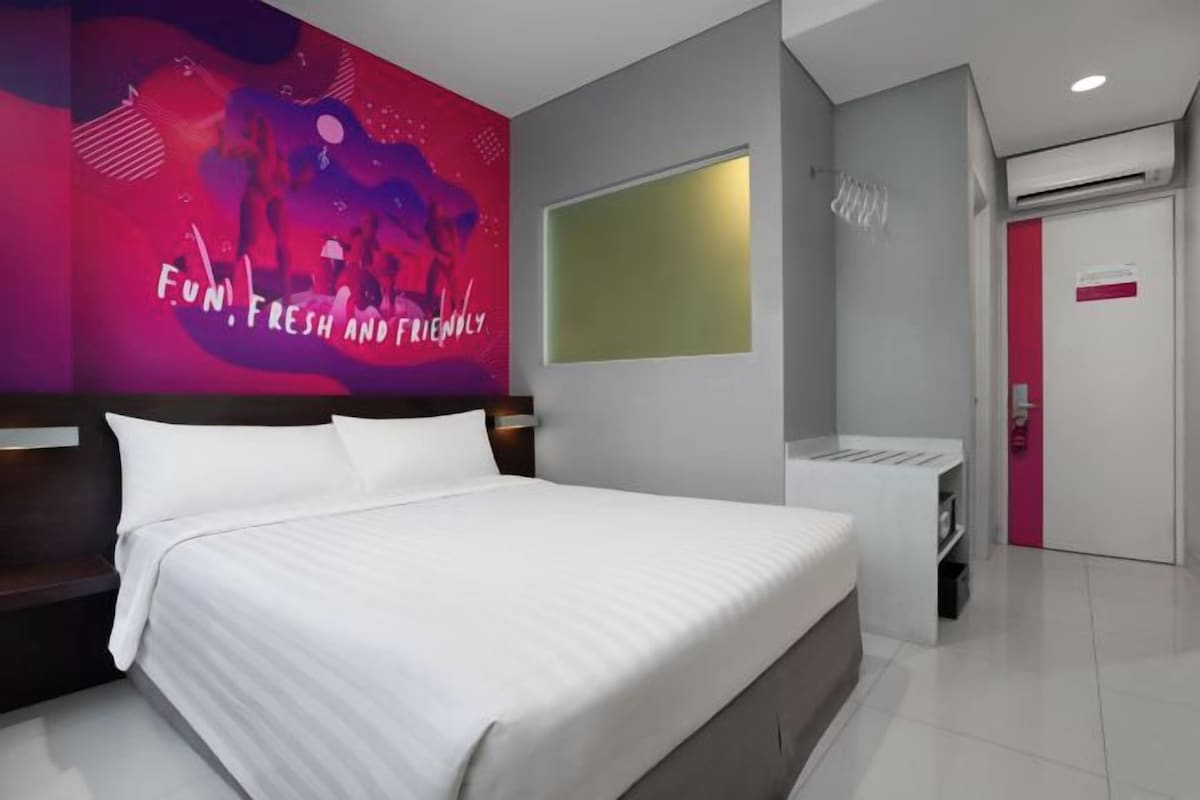A modern hotel room with a large bed, a wall-mounted TV, and a bright red accent wall.