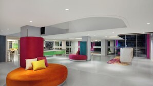 Un lobby moderno con una zona de estar curva color naranja, un pilar rojo y un pilar color turquesa.