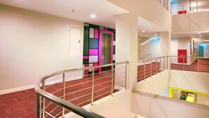 Un interior de varios niveles con una escalera curva, barandillas de metal y un detalle rojo.