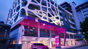 Un edificio moderno con una fachada geométrica distintiva y una entrada visible, con un coche estacionado afuera.