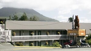 A motel with a bear statue in front, a covered parking area, and a mountain in the background. - Pacific Rim Motel (Ucluelet)