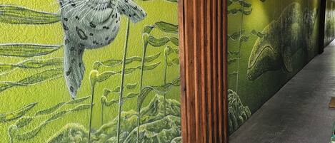 Un pasillo con un mural de una jirafa y un elefante, paneles de madera y suelo de hormigón.