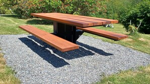 A picnic table with benches in a grassy area with trees and shrubs in the background. - Pacific Rim Motel (Ucluelet)