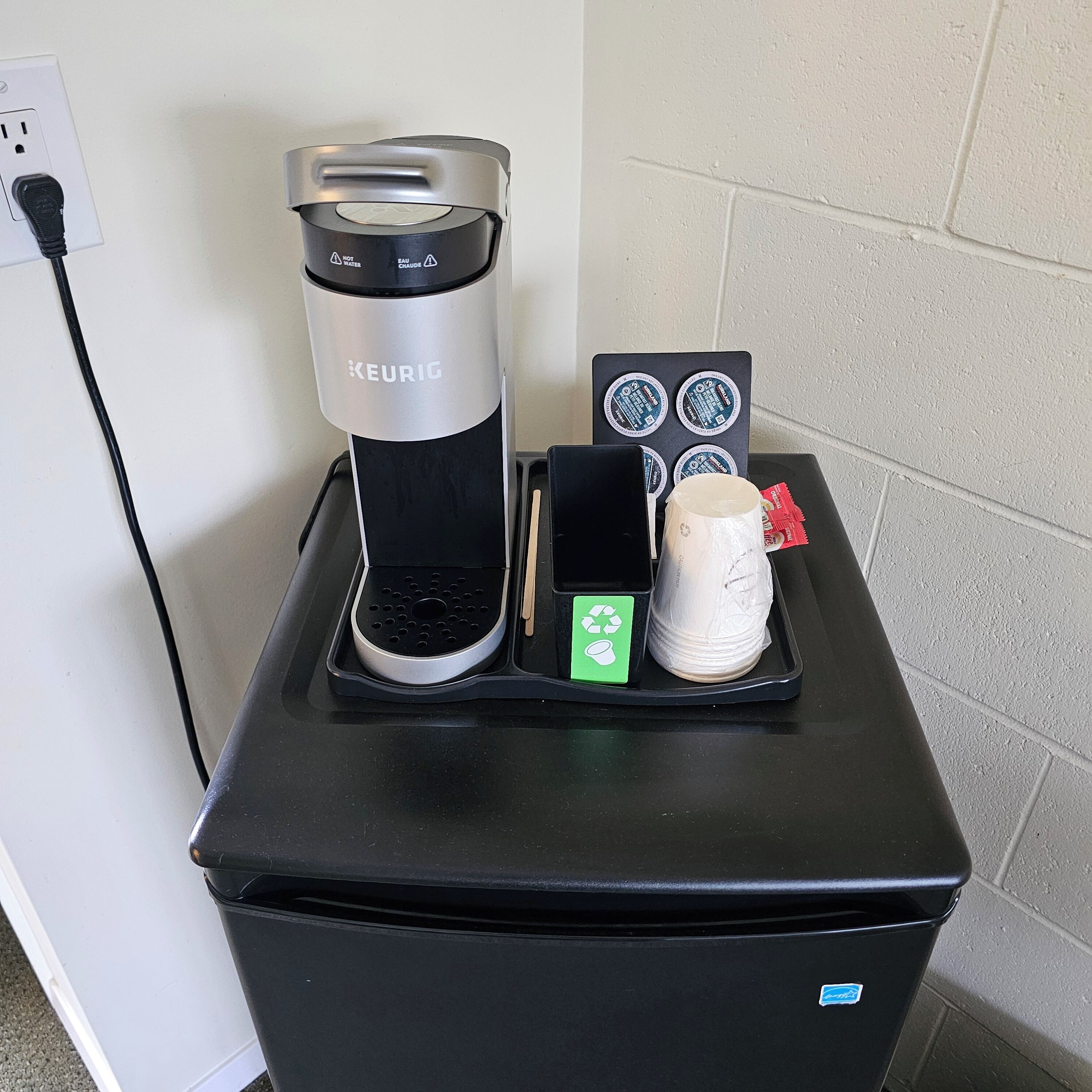 En Keurig kaffemaskine på en sort bordplade med kaffekapselholder, en genanvendelig kop og en papirkurv.