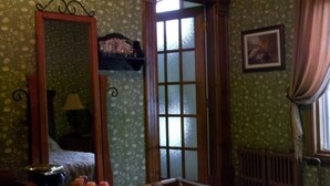 A room with floral wallpaper, a wooden bed, a mirror, a radiator, and a window with curtains. - Auberge Le St-Gab (Saint-Gabriel)