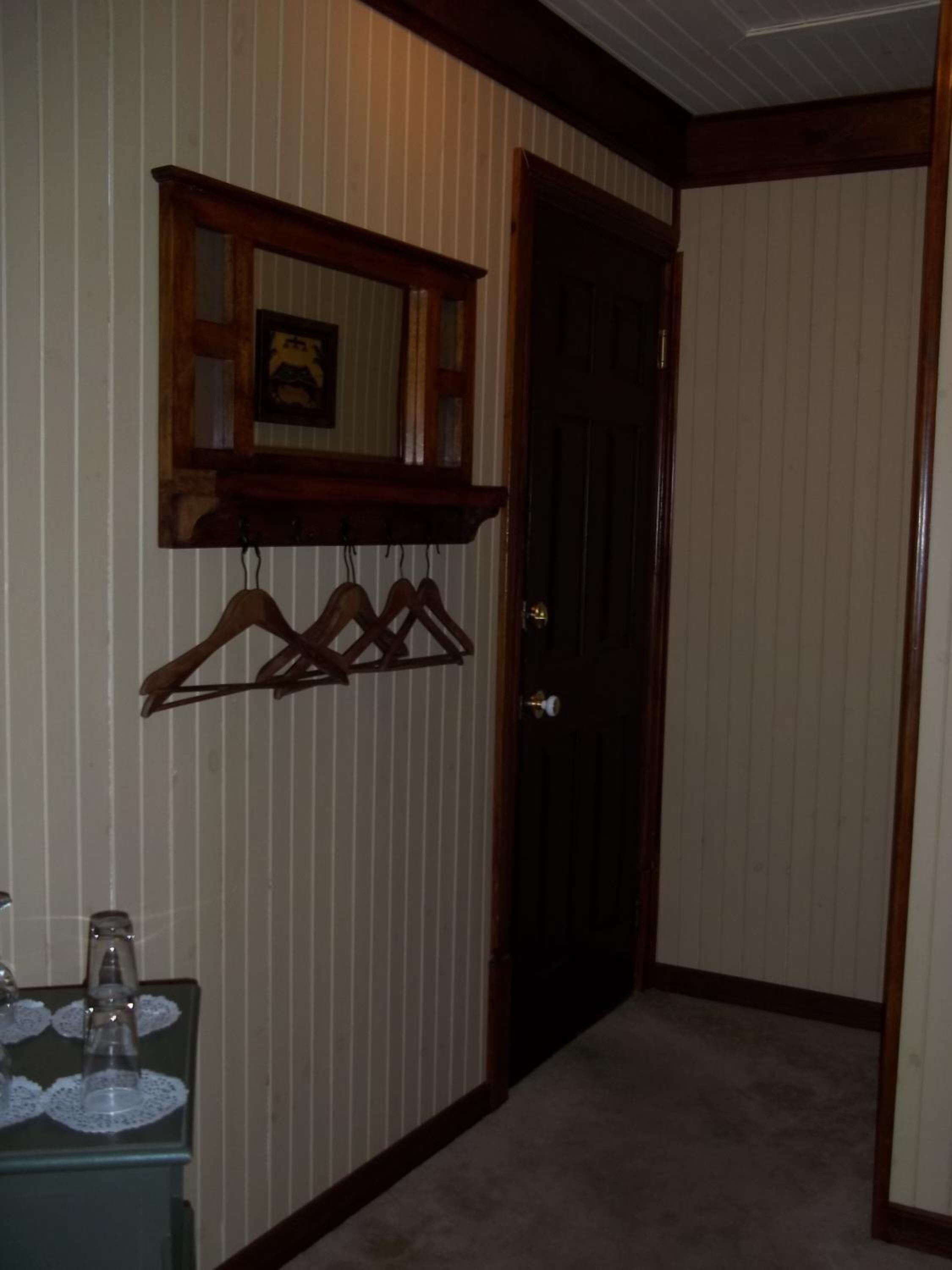 A hallway with a coat rack, a door, and a small table with glasses.