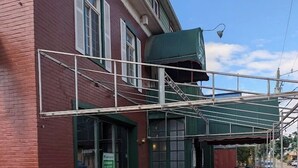 A brick building with a wooden deck, a covered outdoor seating area, and a green awning. - Auberge Le St-Gab (Saint-Gabriel)