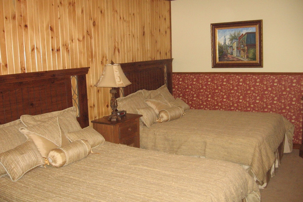 A room with two beds, wooden headboards, a nightstand with a lamp, and a floral-patterned wall.