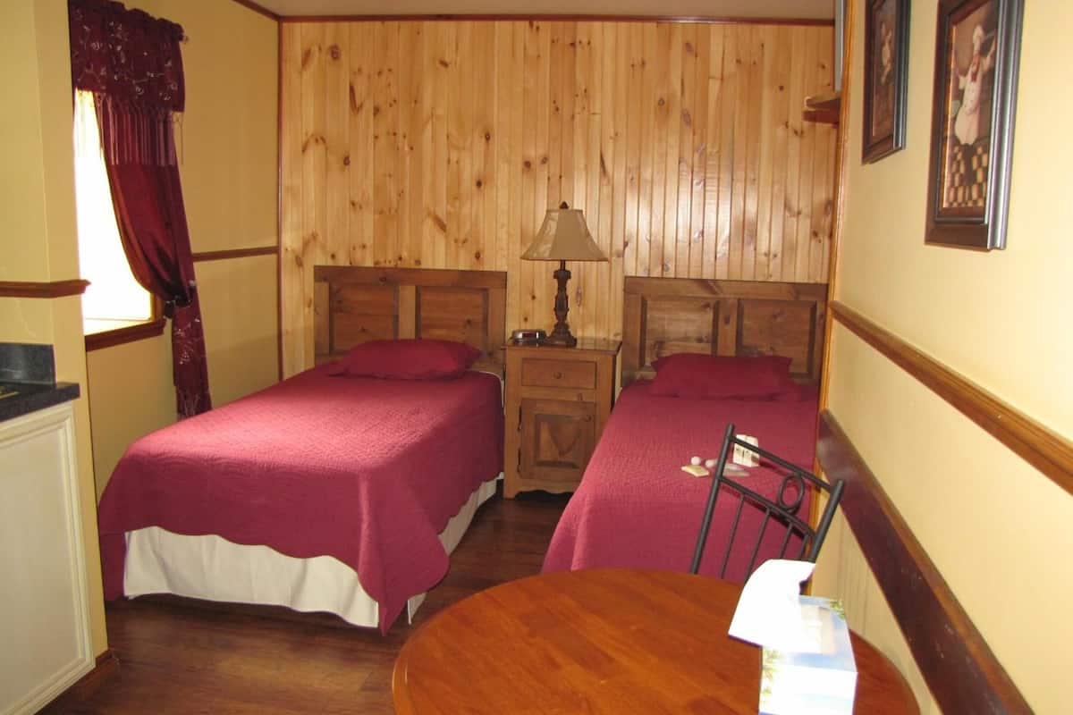 A room with two wooden beds, a round wooden table, and a nightstand with a lamp.
