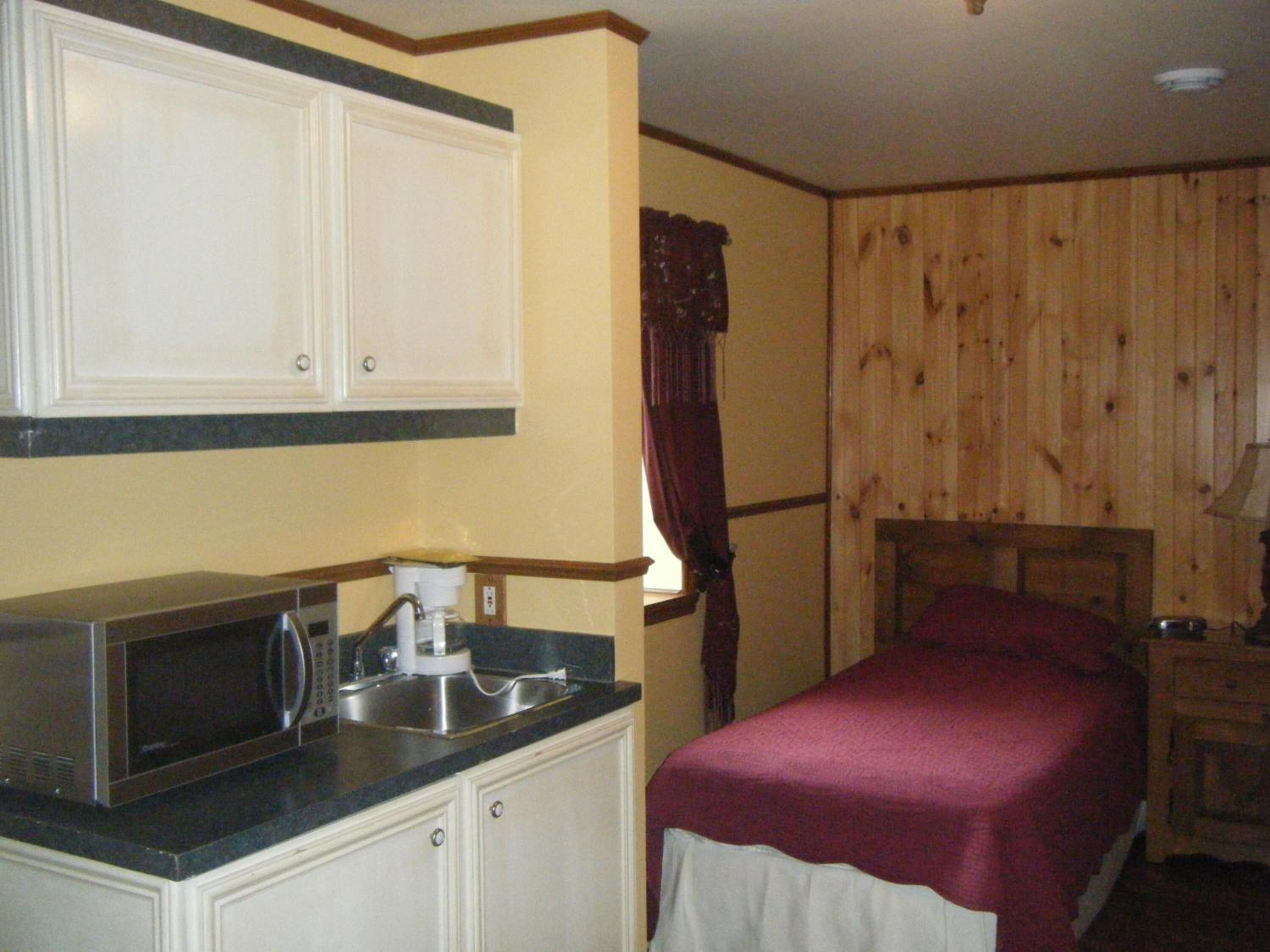 Un dormitorio con cama, cabecera de madera, mesita de noche y microondas integrado.