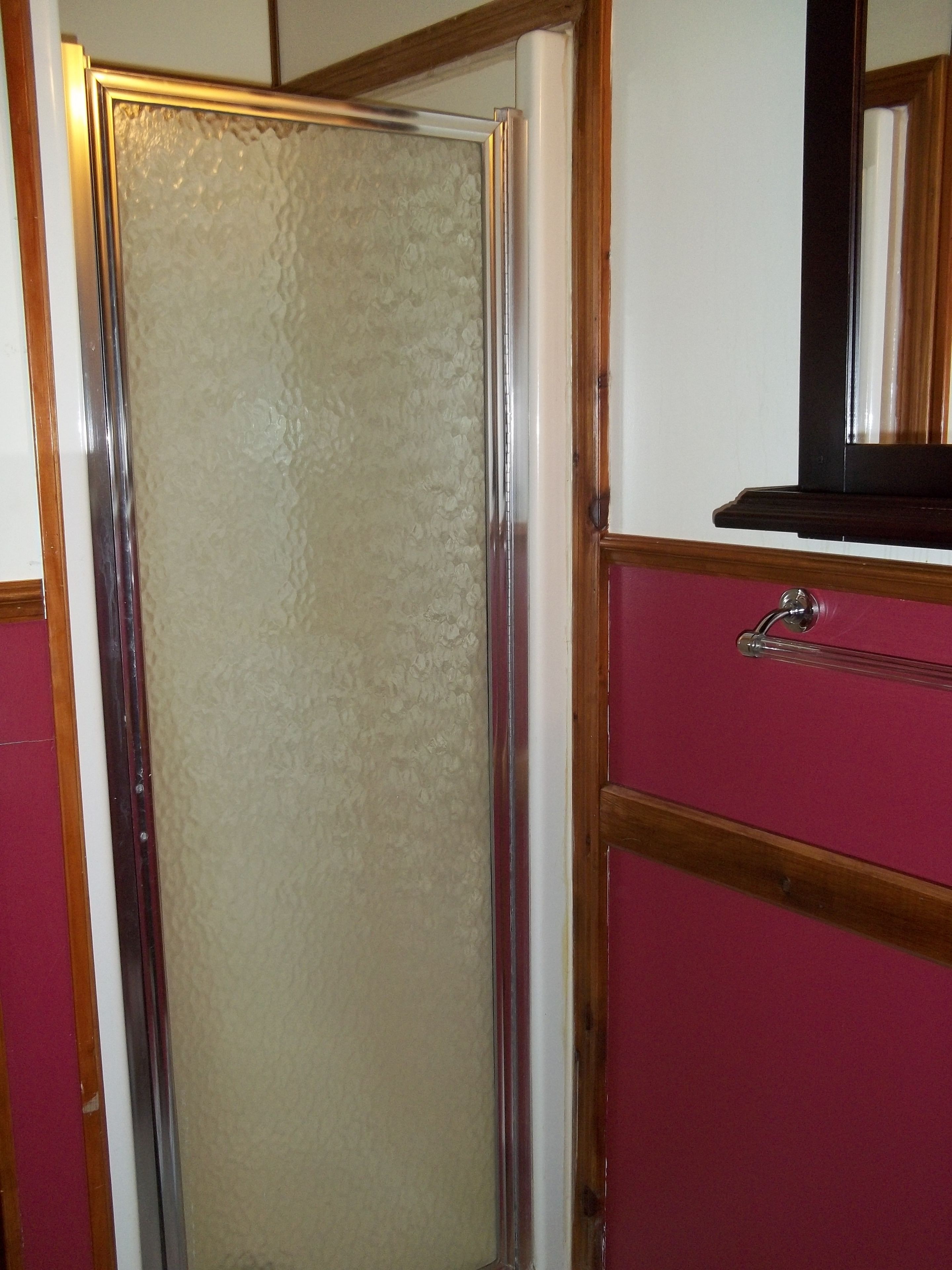 A bathroom with a glass shower enclosure, a wooden-framed mirror, and a pink vanity with a chrome faucet.