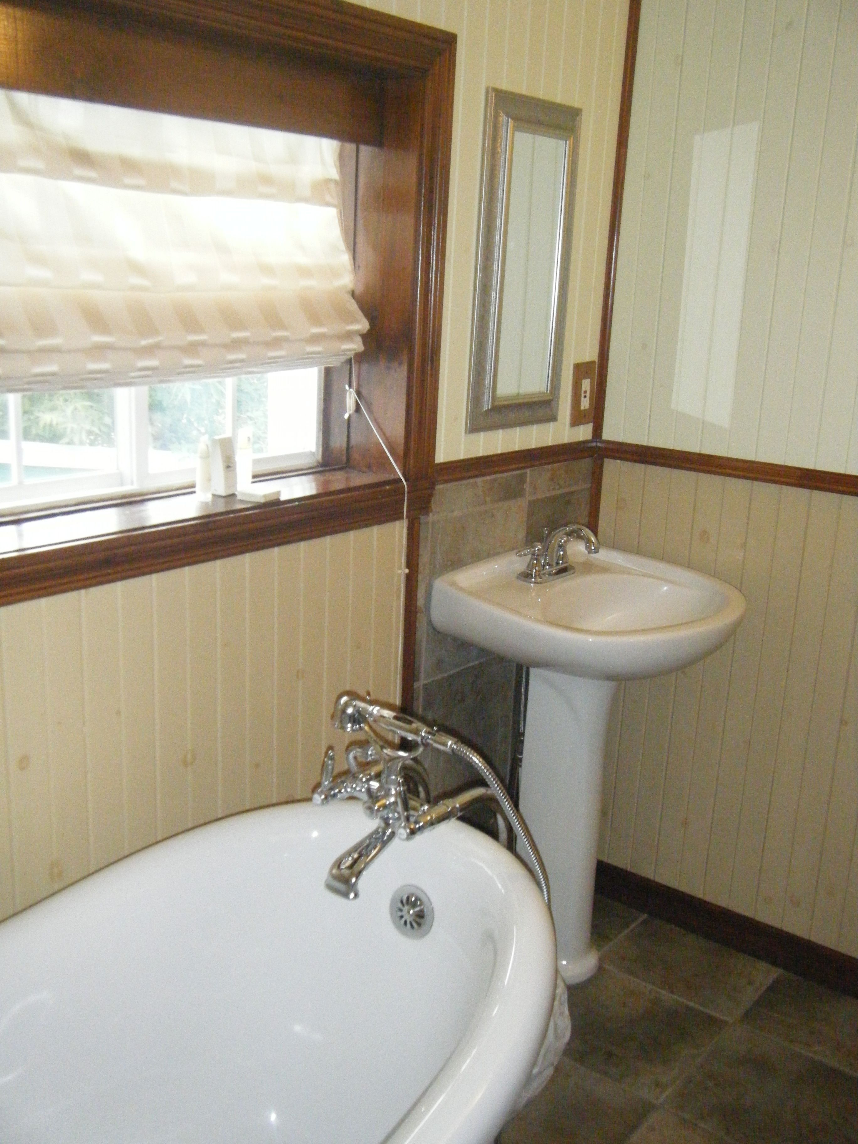 A bathroom with a bathtub, a sink, and a window with a blind.