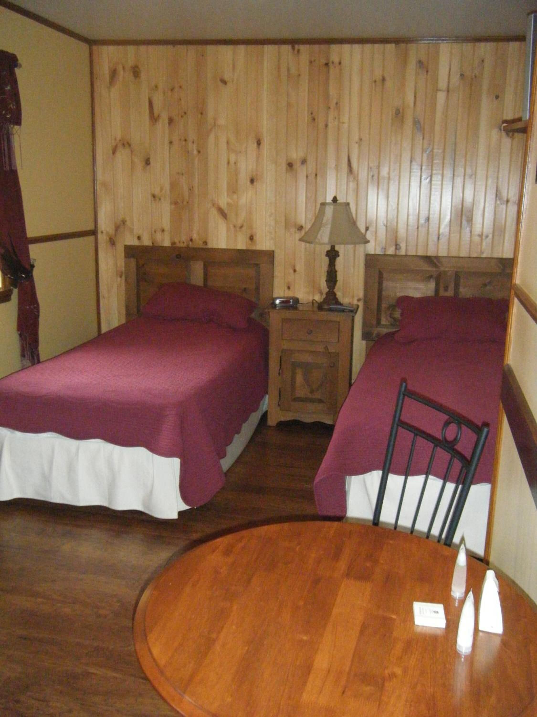 A room with two beds, a wooden table, and a nightstand with a lamp.